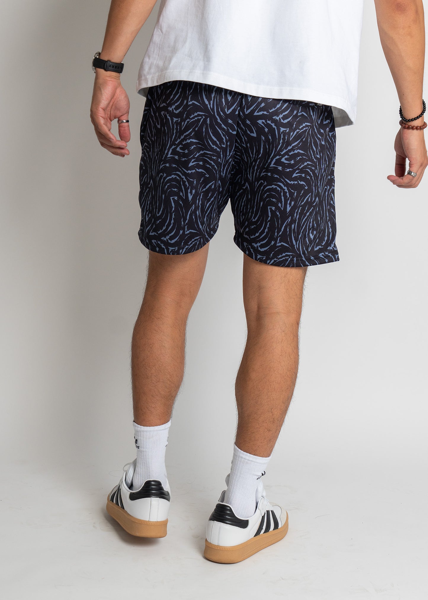 Person wearing navy shorts with white pattern, white shirt, and black and white sneakers on a plain background
