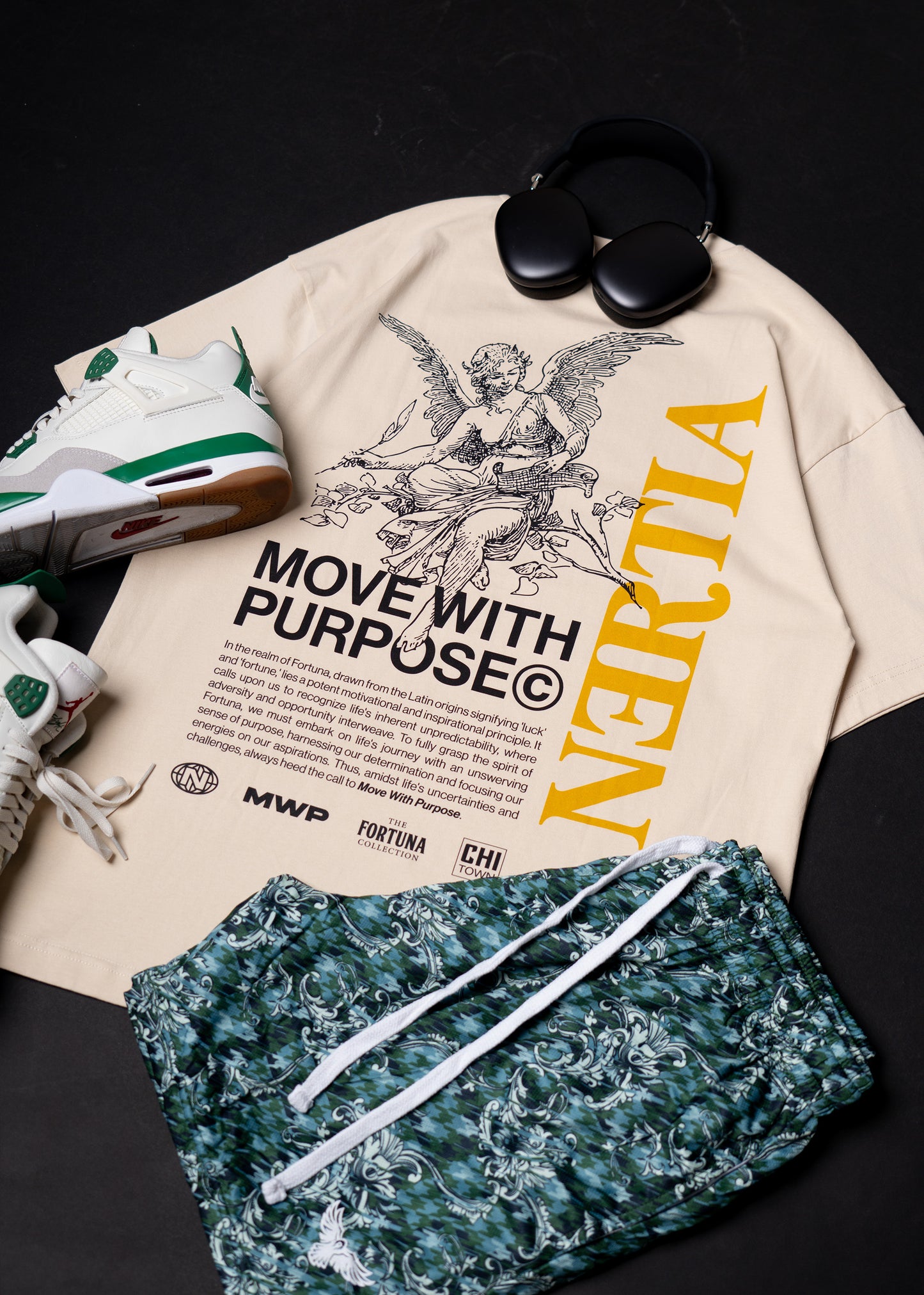 Beige sweatshirt with graphic design and text, green shorts, and sneakers on a dark surface