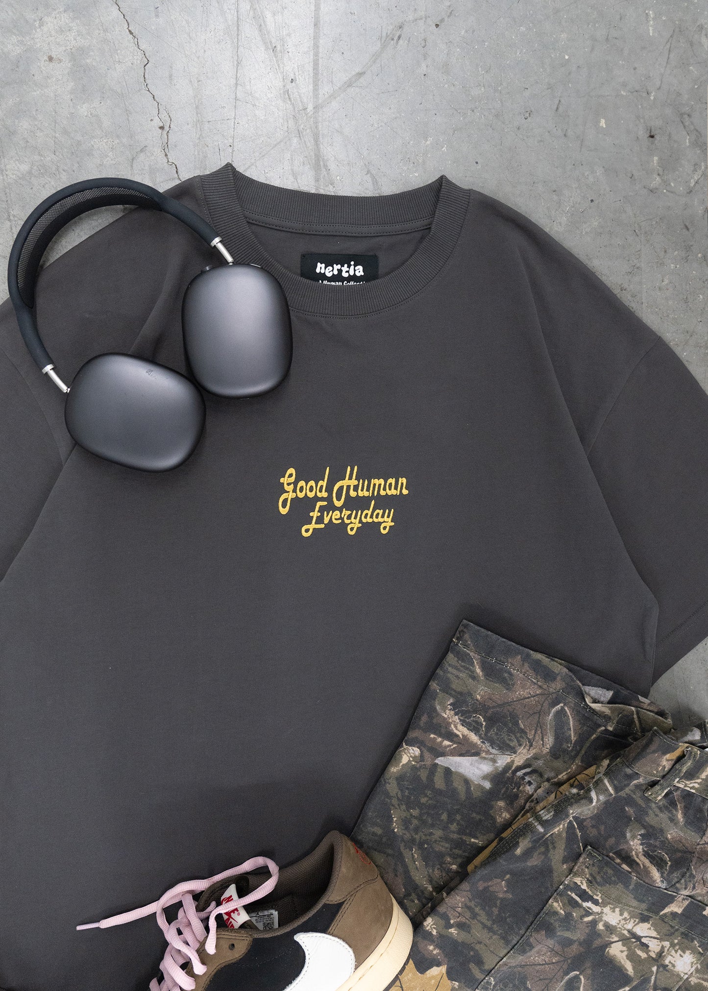 Black sweatshirt with 'Good Human Everyday' text, headphones, and camouflage pants on a gray surface