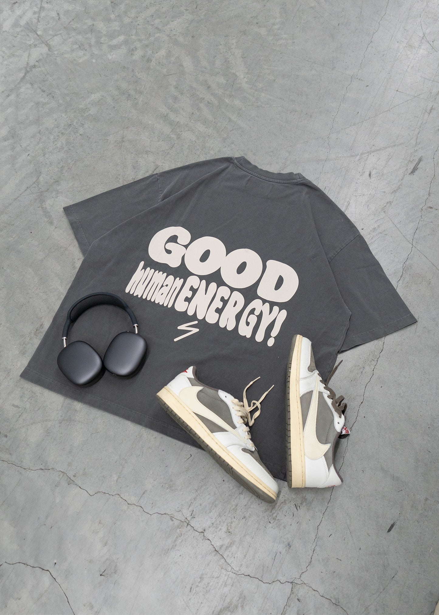 Black t-shirt with 'GOOD MATHMATIC ENERGY!' text, sneakers, and headphones on a gray concrete surface.