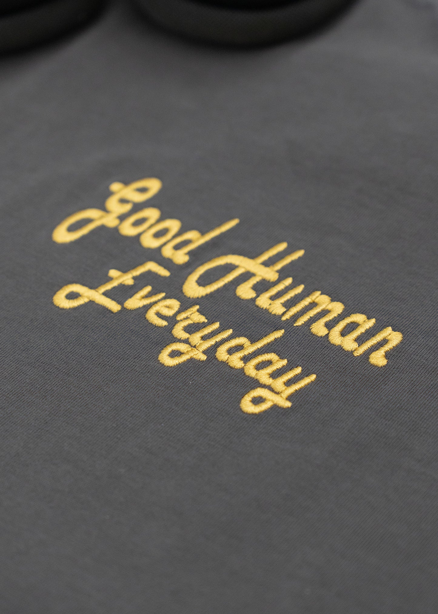 Text 'Good Human Everyday' embroidered on a dark fabric background