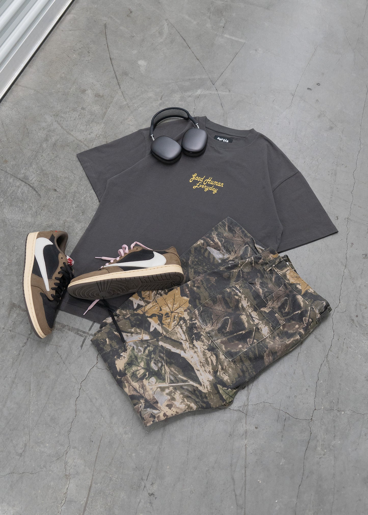 Black t-shirt with yellow text, camouflage pants, and sneakers on a gray concrete floor.