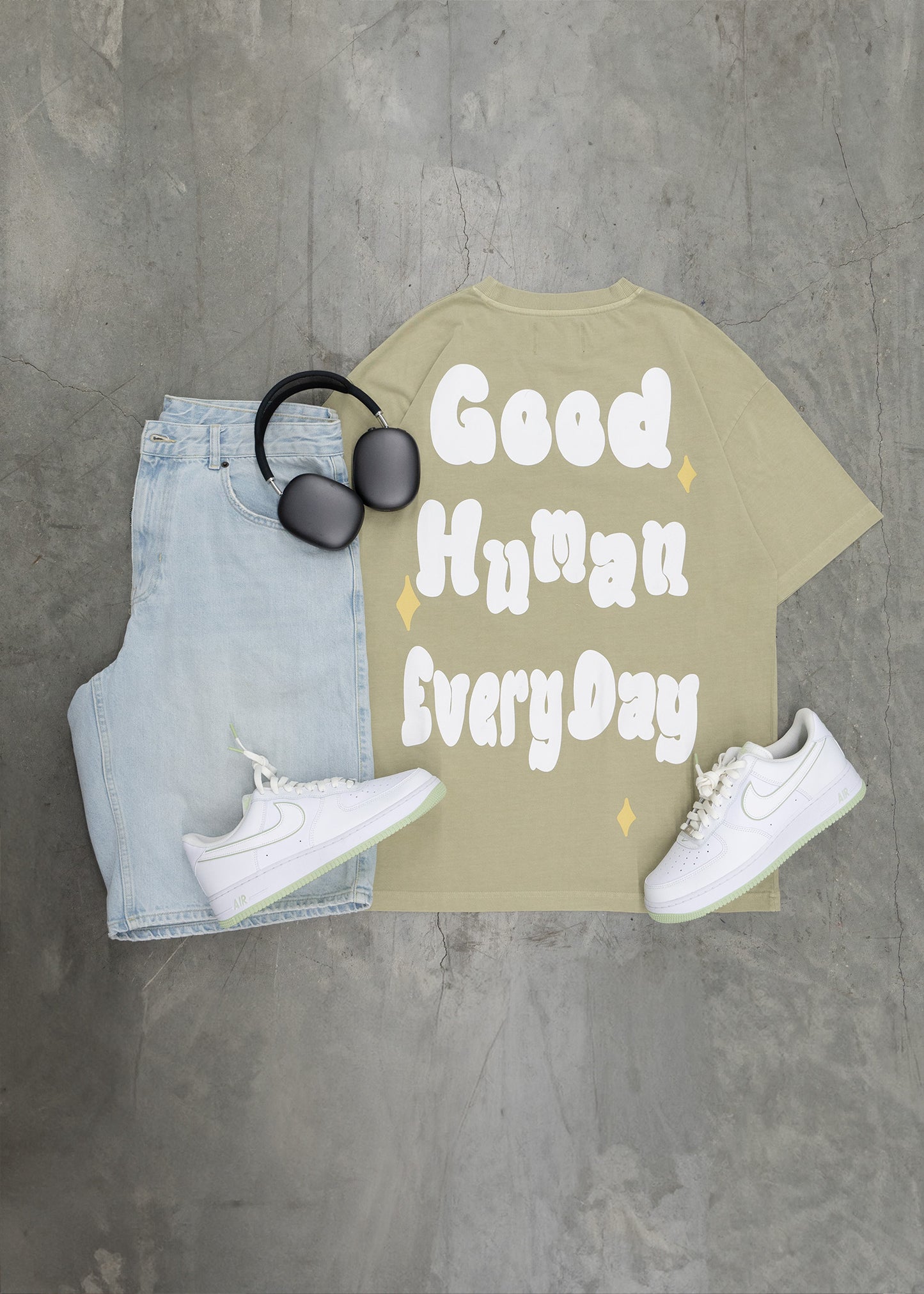 T-shirt with 'Good Human Every Day' text, jeans, sunglasses, and sneakers on a gray surface