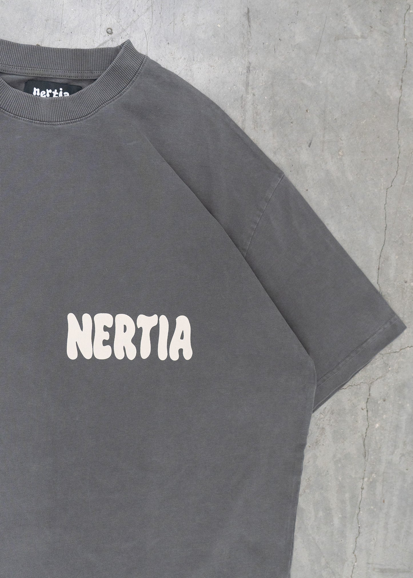 Gray t-shirt with 'NERTIA' logo on a concrete surface