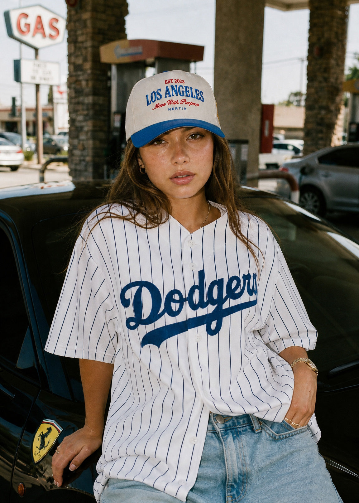 Person wearing a Los Angeles Dodgers jersey and cap in front of a gas station.
