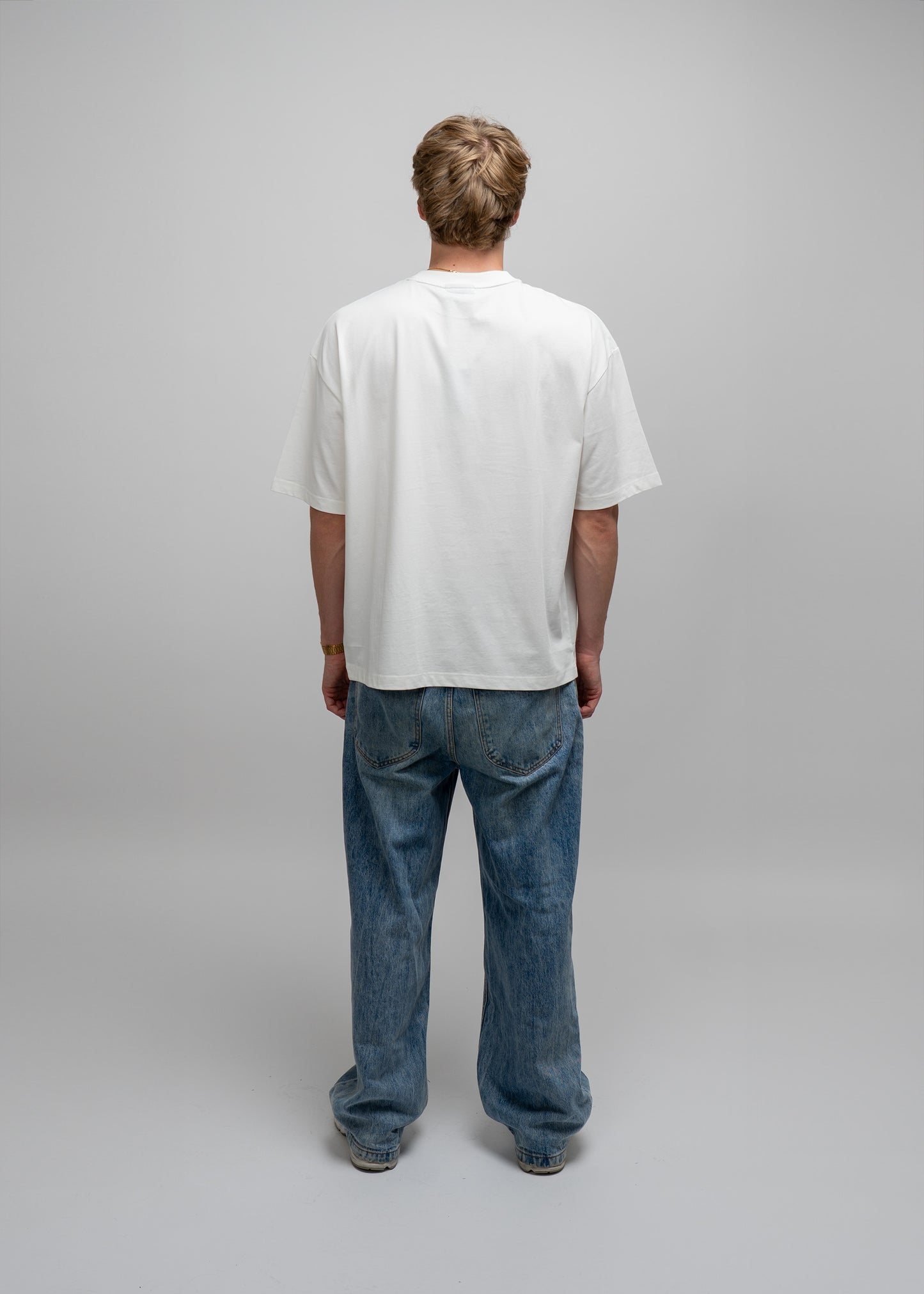 Person wearing a plain white t-shirt and blue jeans on a gray background