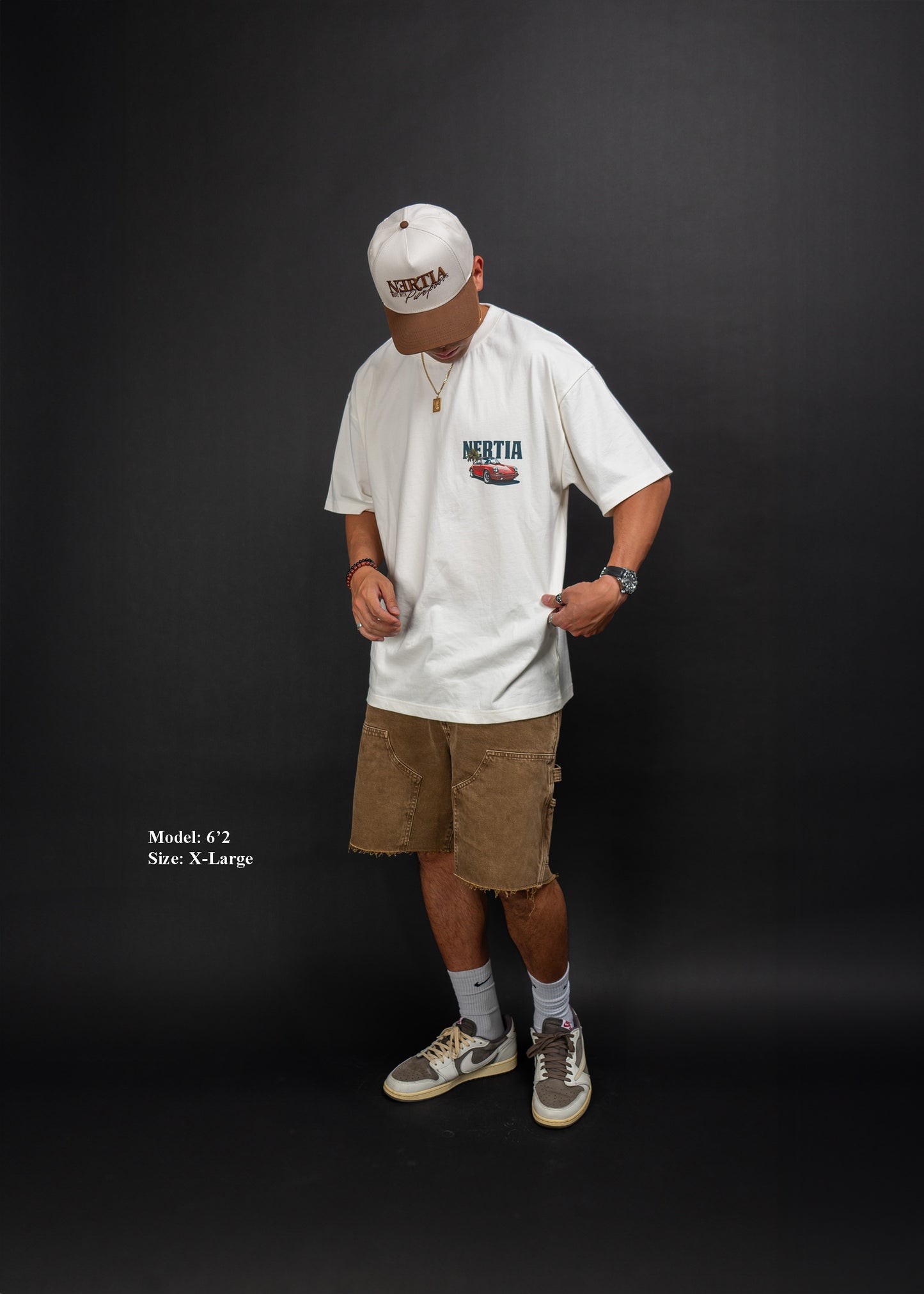 Person wearing a white t-shirt with text and graphics, brown shorts, and a white cap on a black background