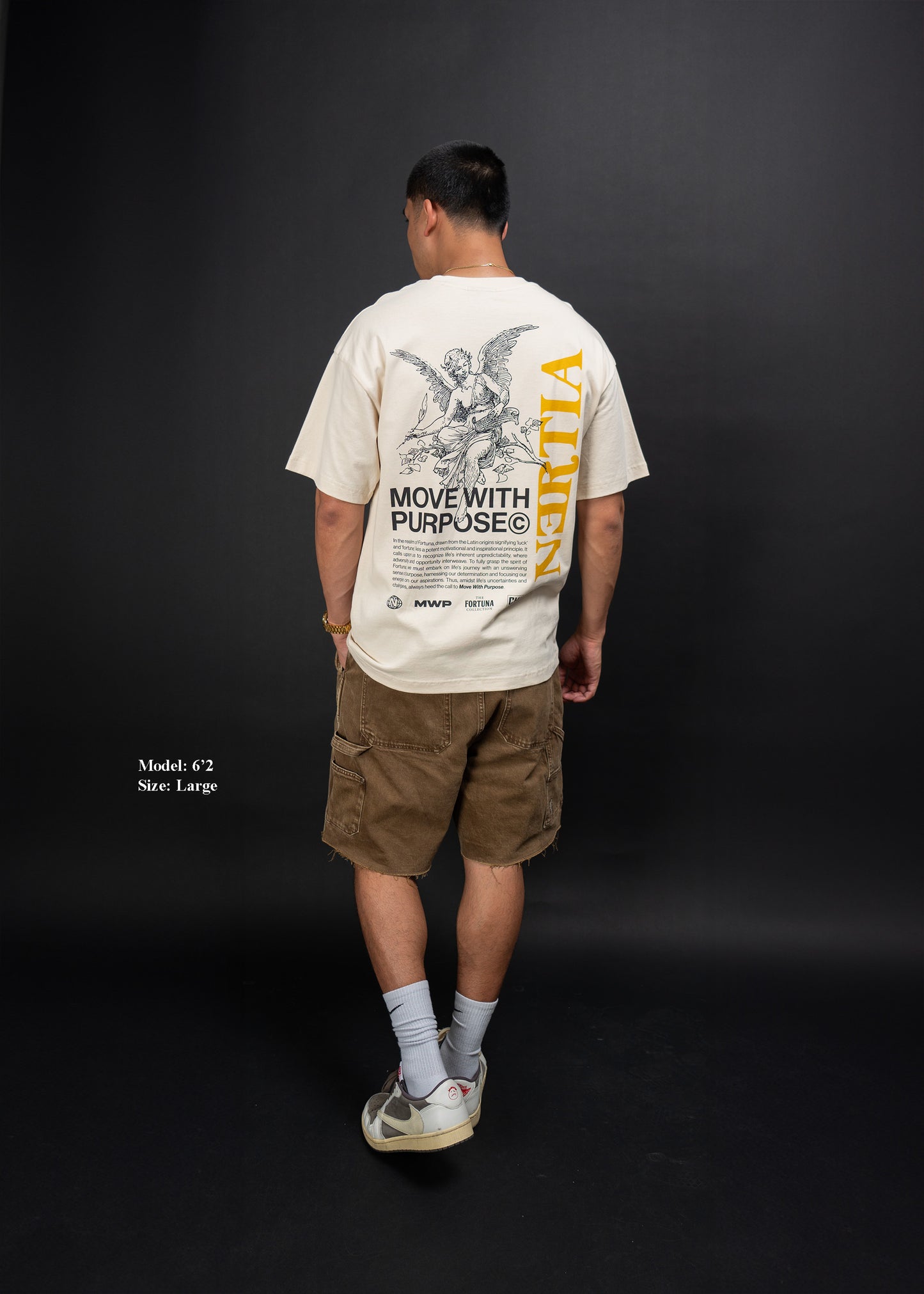 Person wearing a beige t-shirt with text and graphics on the back, standing against a black background