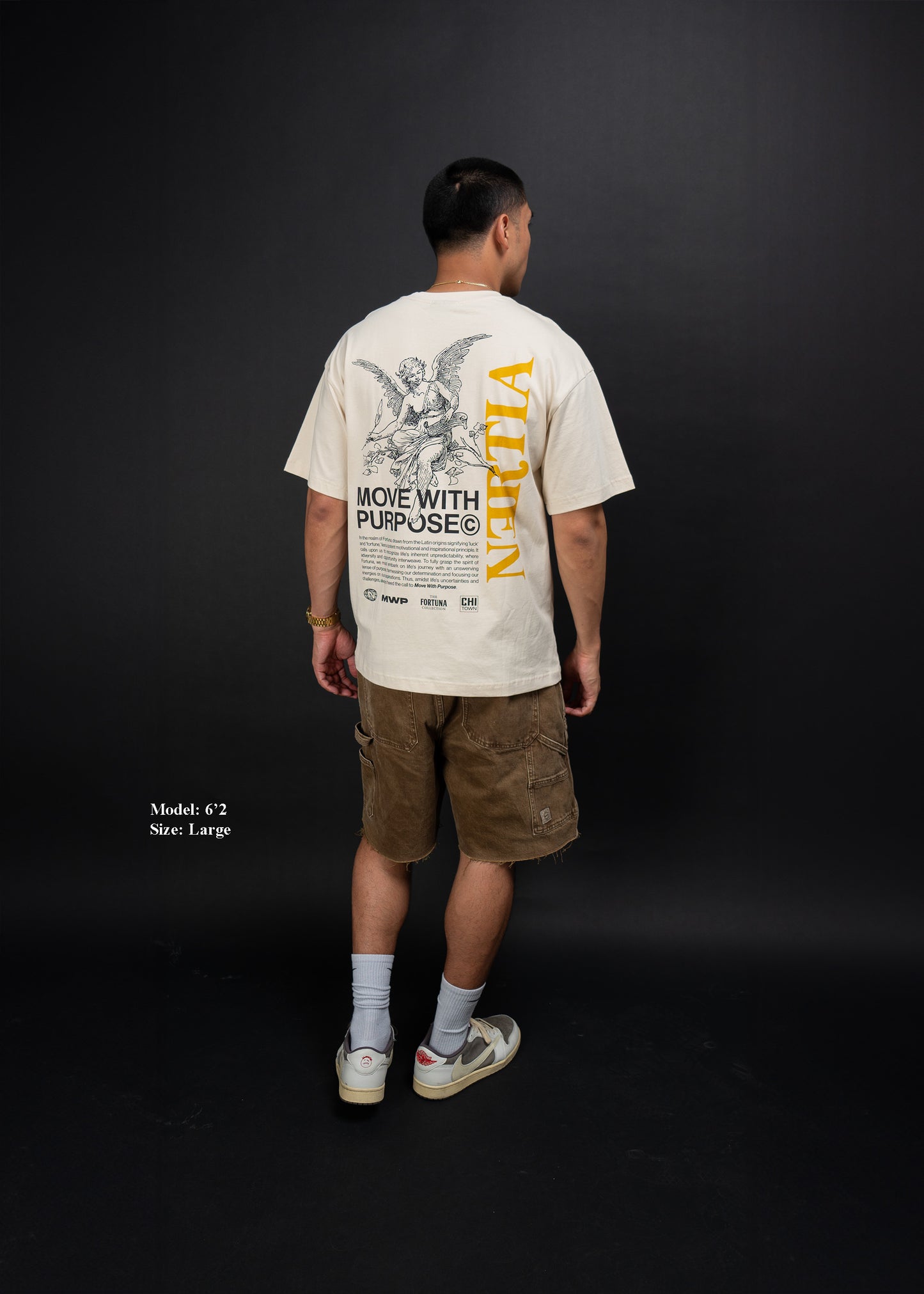 Person wearing a beige t-shirt with text and graphics on the back, standing against a black background.