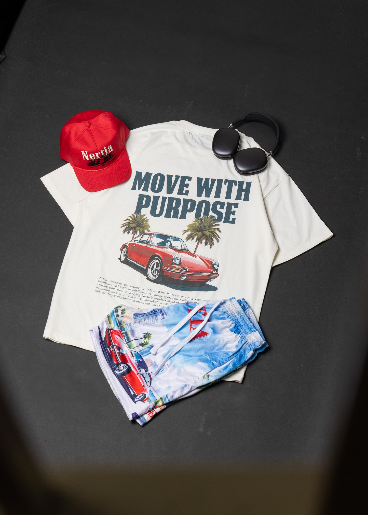 White t-shirt with car graphic and text, red cap, and folded fabric on a dark surface