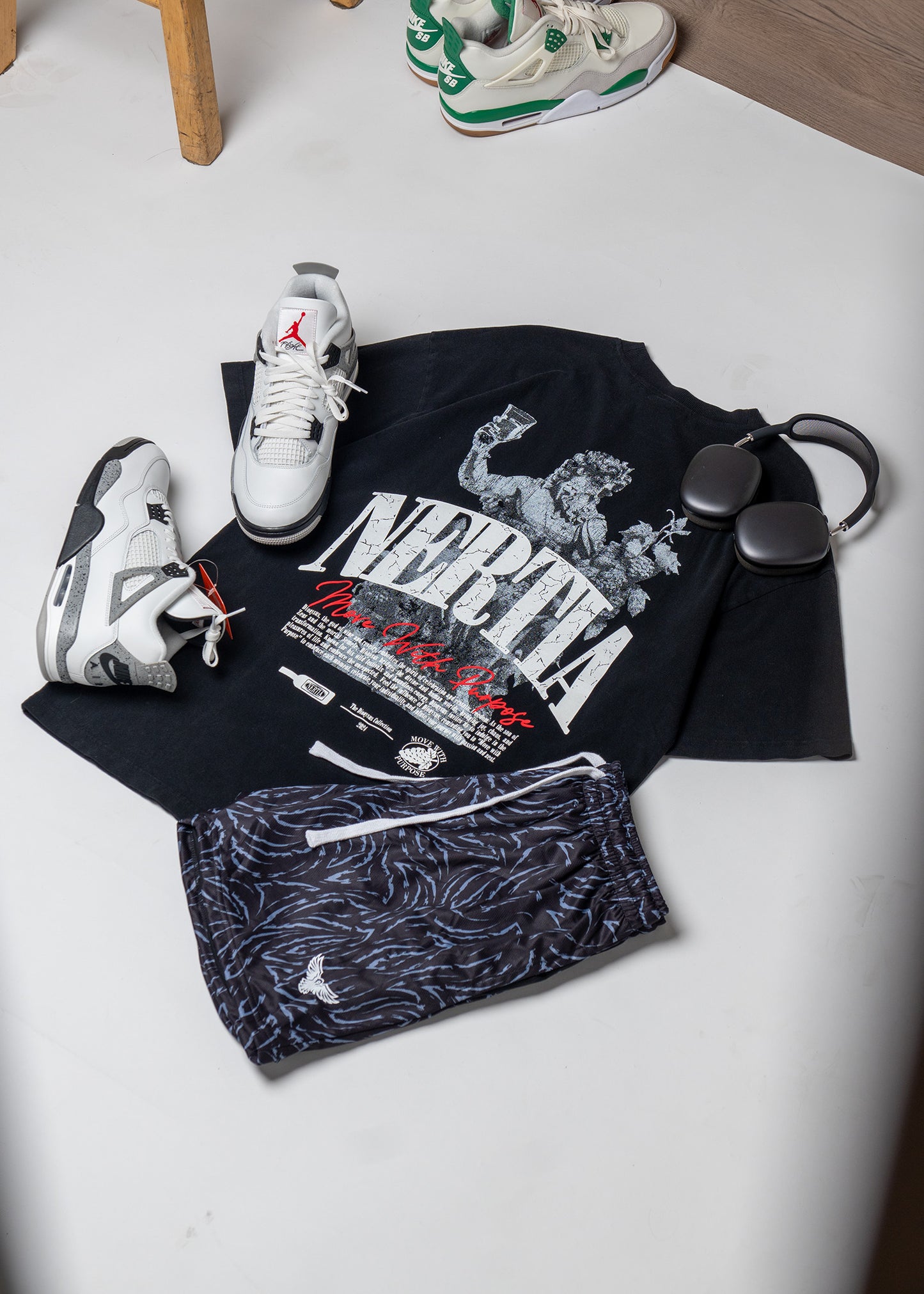 Black t-shirt with graphic design, patterned shorts, and sneakers on a light surface