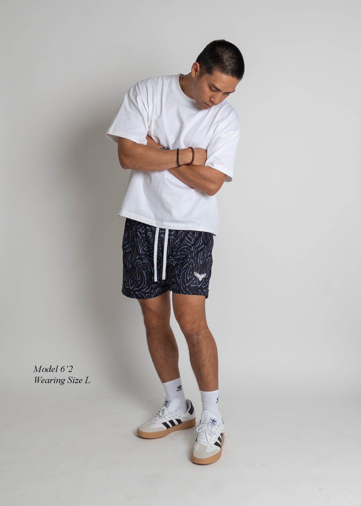 Man wearing a white t-shirt, black shorts with white drawstring, and white sneakers on a plain background