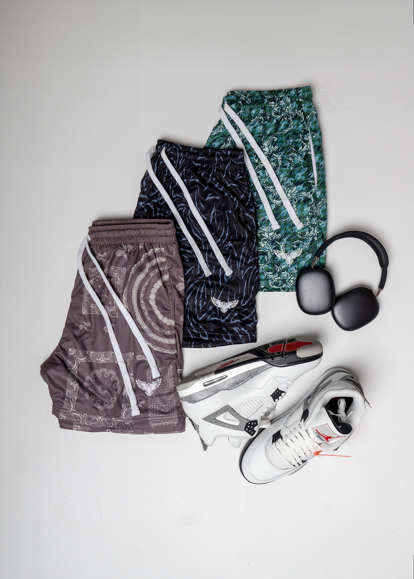 Three pairs of patterned shorts and a pair of sneakers on a light gray background