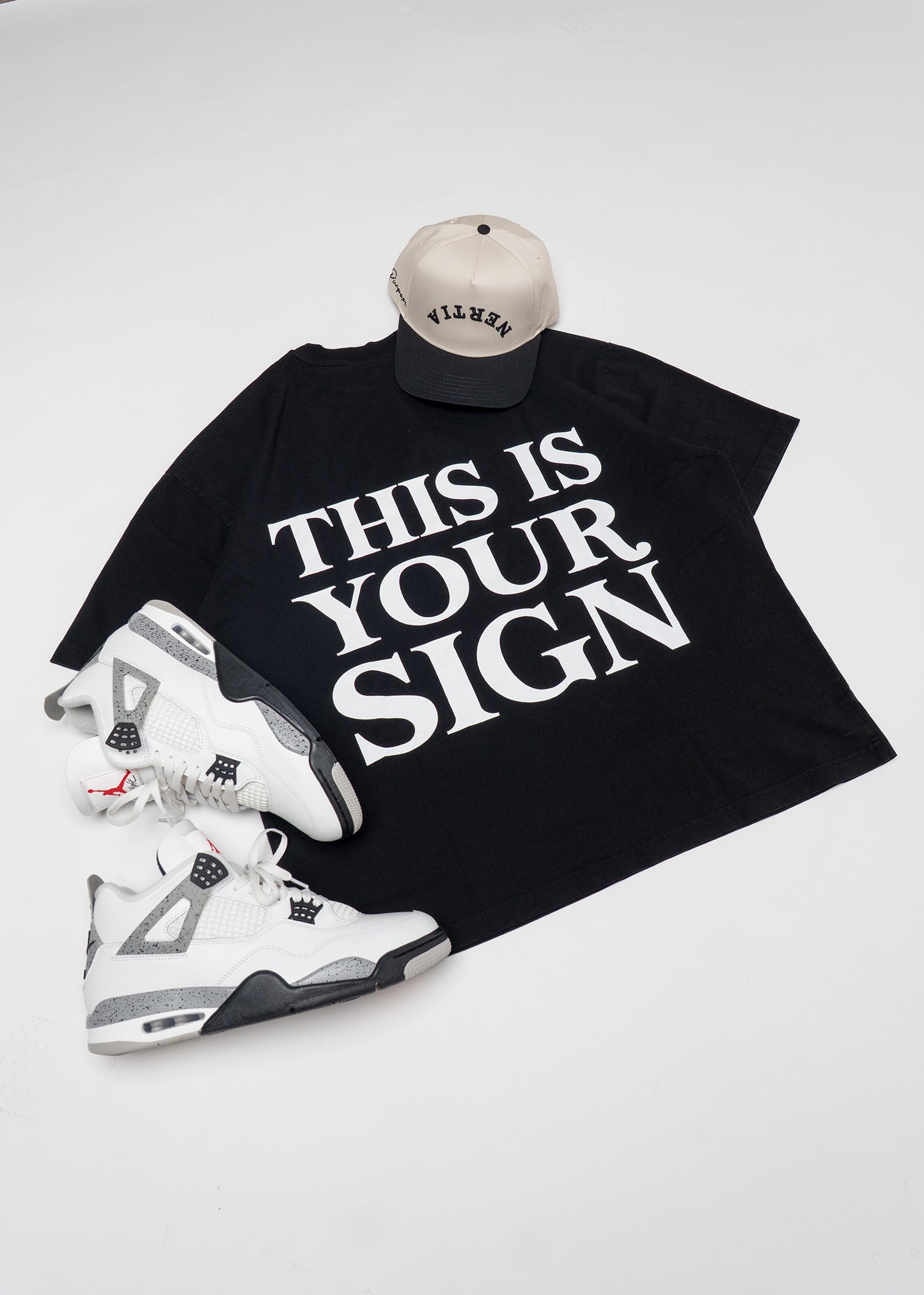 Black t-shirt with 'THIS IS YOUR SIGN' text, white sneakers, and beige cap on a light gray background