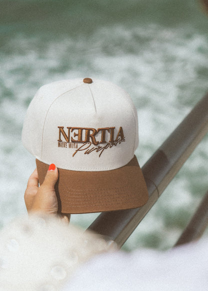 White and brown cap with 'Neirtia' branding held by a hand against a blurred natural background