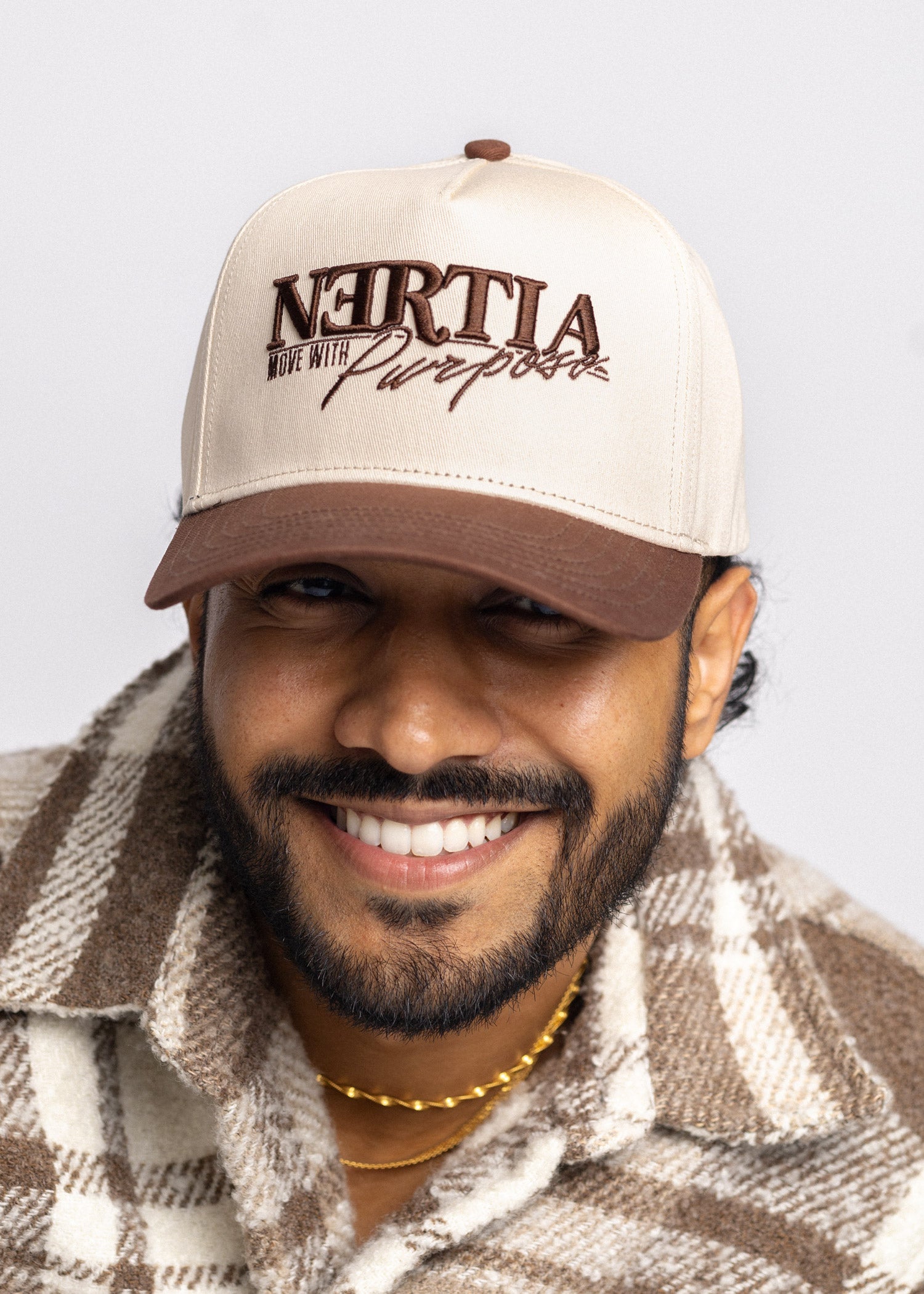 Man wearing a beige cap with text, smiling against a plain background