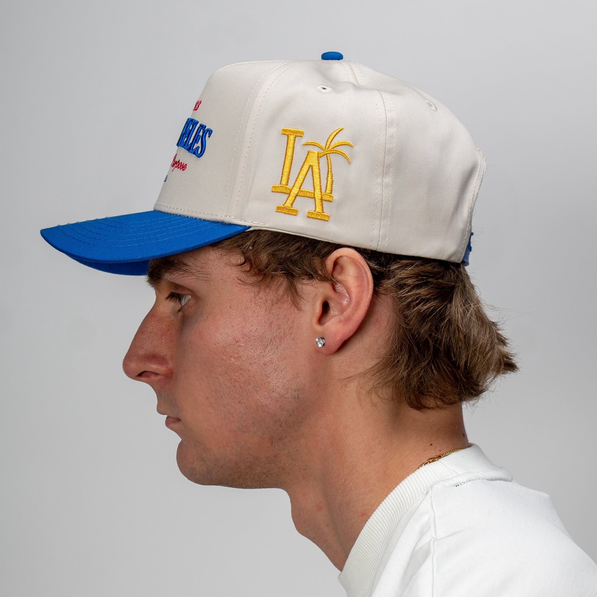 Person wearing a white cap with blue and yellow accents on a plain background