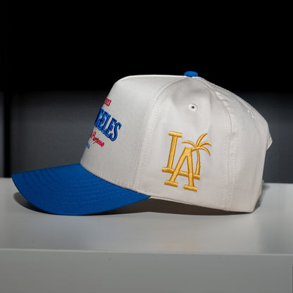 Baseball cap with blue brim and white bill featuring logos on a dark background