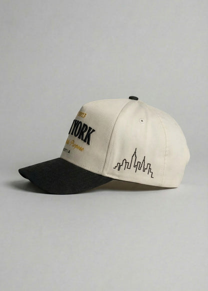 Beige and black cap with city skyline design on a gray background