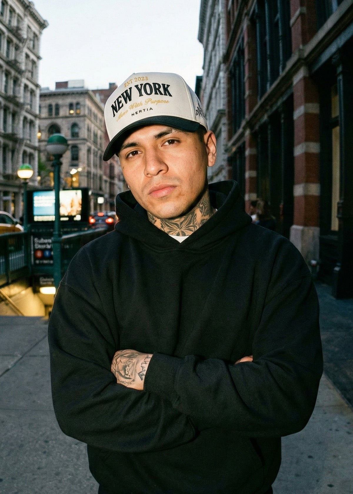 Man wearing a black hoodie and 'New York' cap standing on a city street.