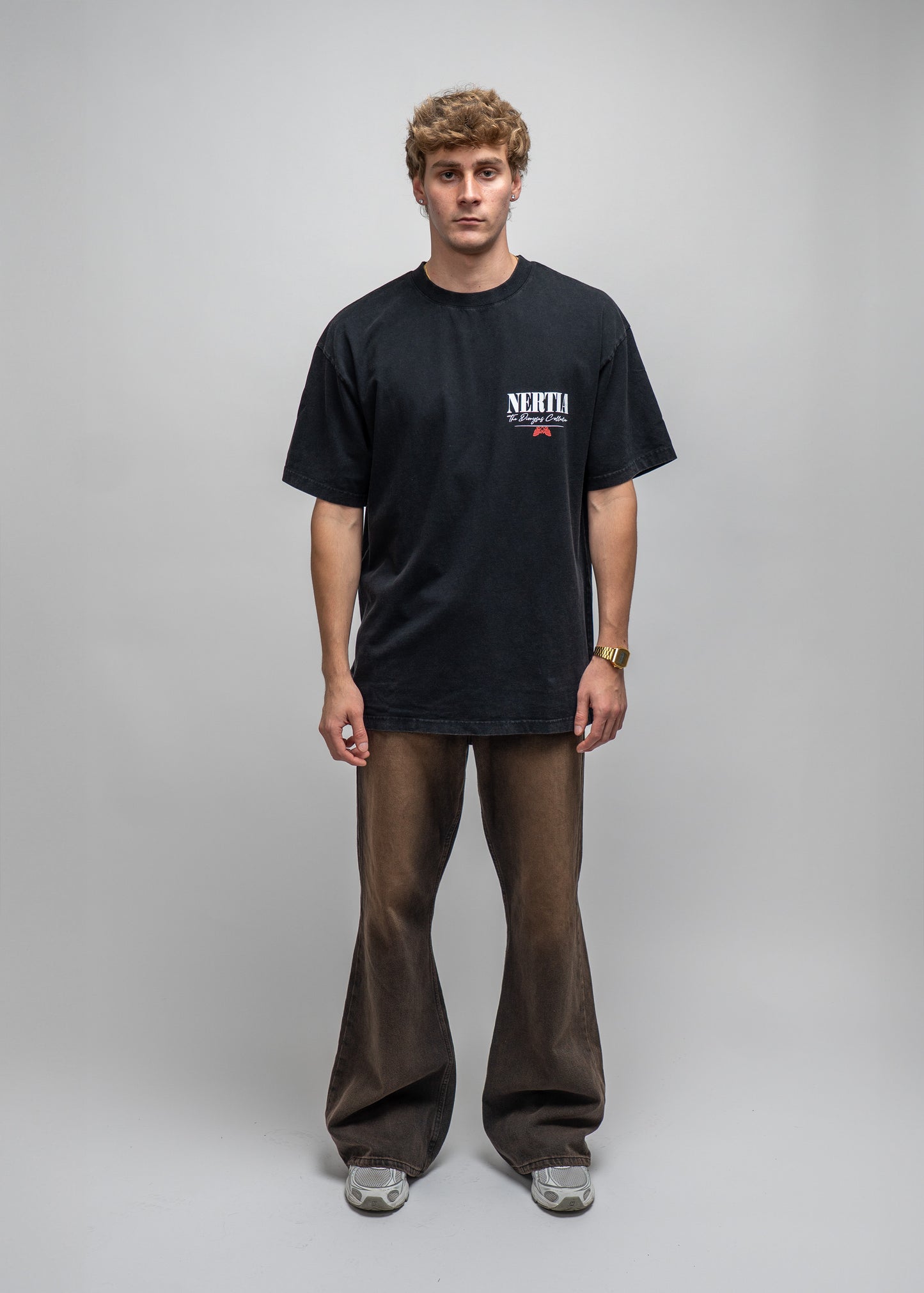 Person wearing a black t-shirt with a logo and brown pants on a gray background