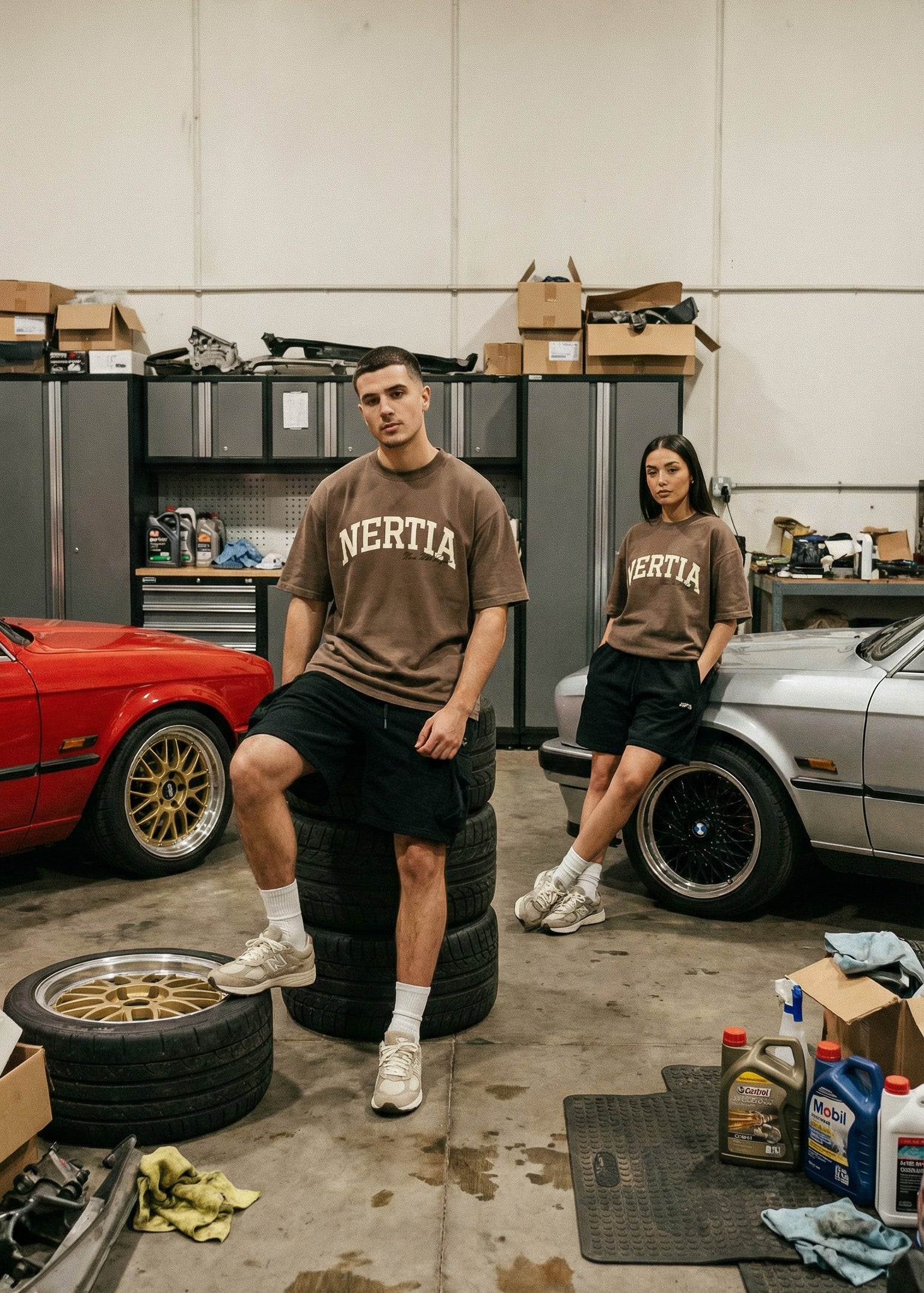 Two people wearing 'Nertia' shirts in a garage with cars and tools.