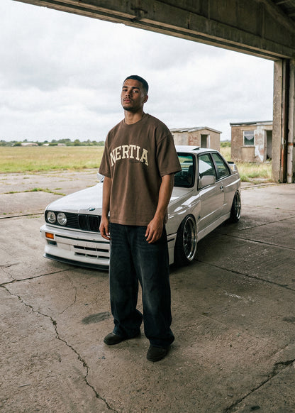 Man standing in front of a white car with 'Nertia' t-shirt in an industrial setting