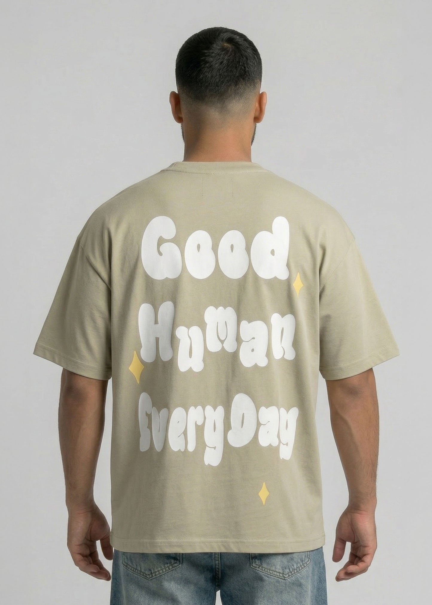 Person wearing a beige t-shirt with 'Good Human Every Day' text on the back against a plain background