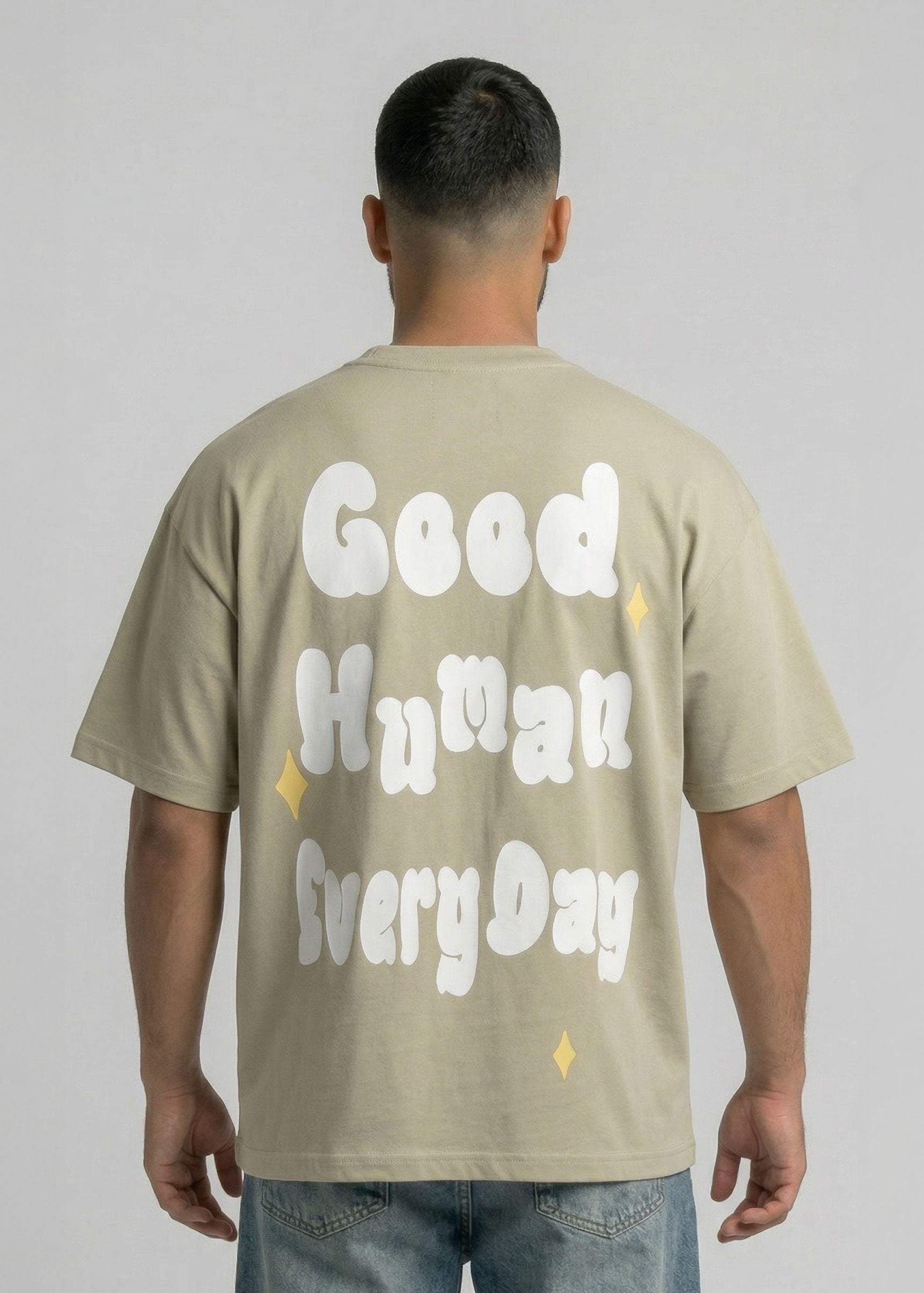 Person wearing a beige t-shirt with 'Good Human Every Day' text on the back against a plain background