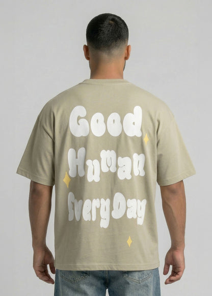 Person wearing a beige t-shirt with 'Good Human Every Day' text on the back against a plain background