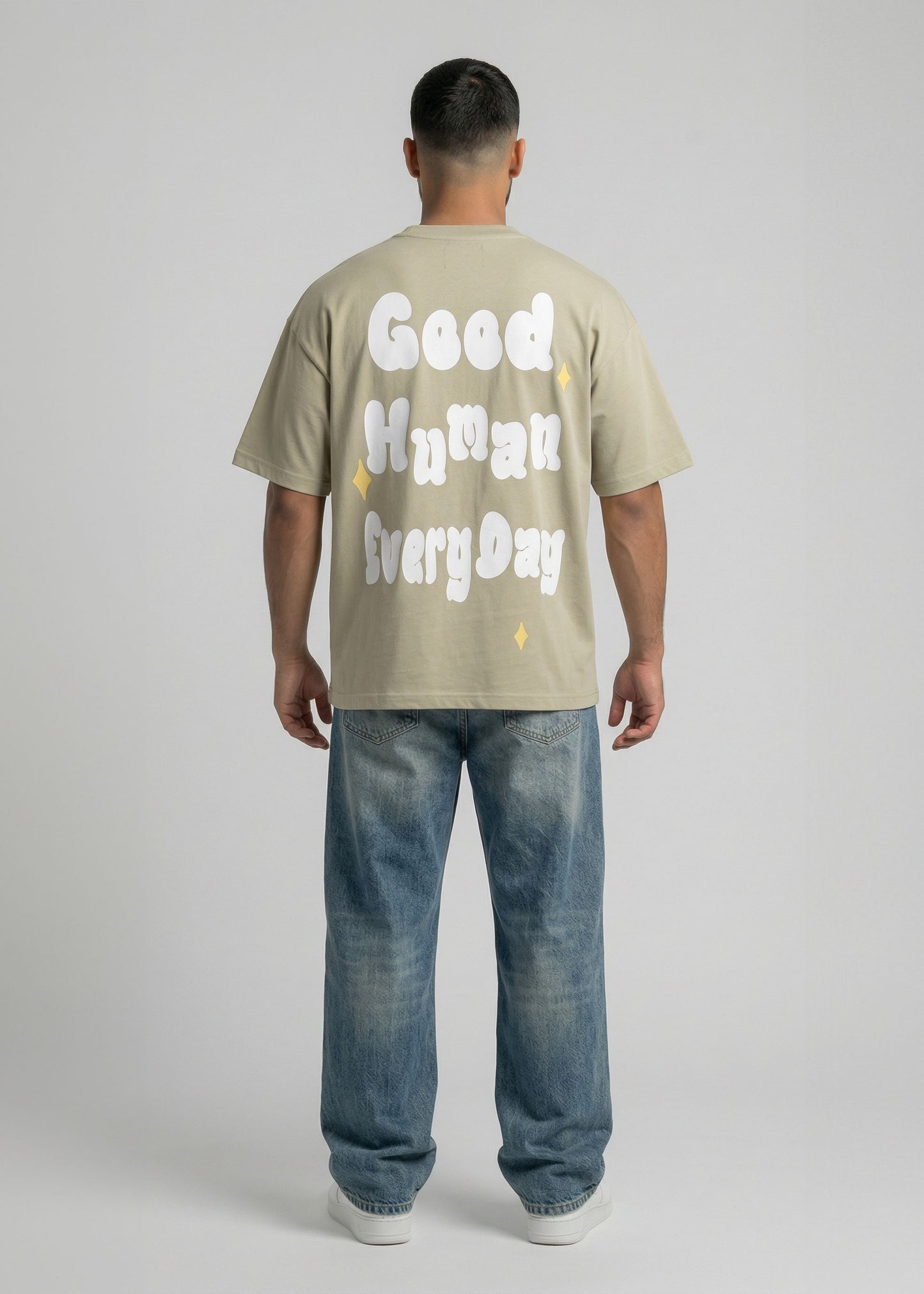 Person wearing a beige t-shirt with text and blue jeans on a plain background