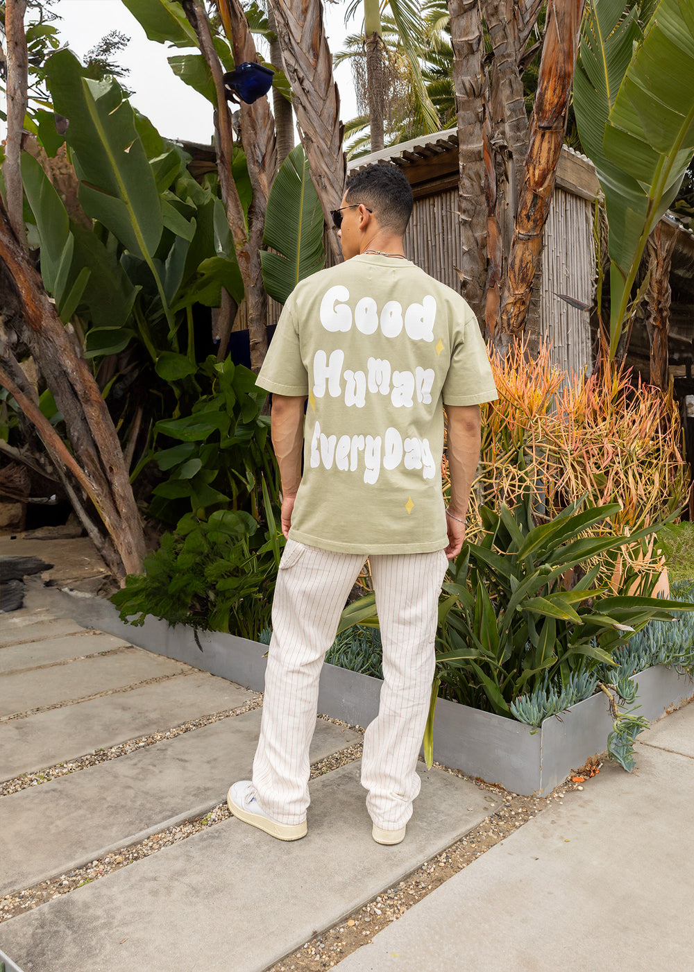 Person wearing a light green t-shirt with text, standing in a garden setting.