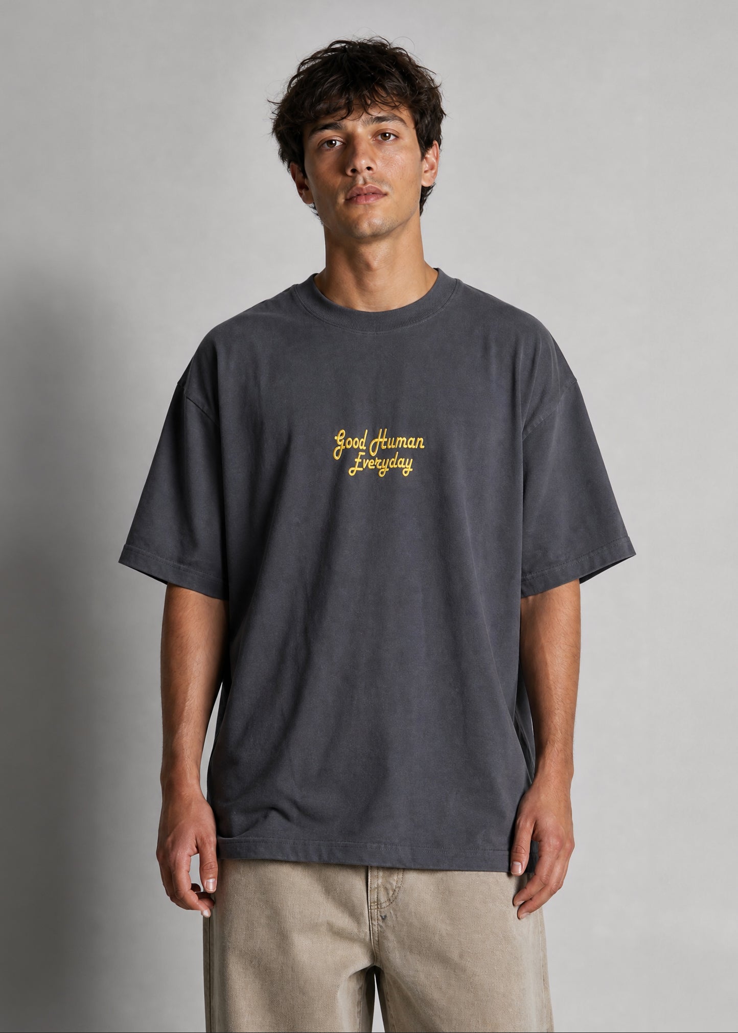 Man wearing a dark gray t-shirt with yellow text on a plain background