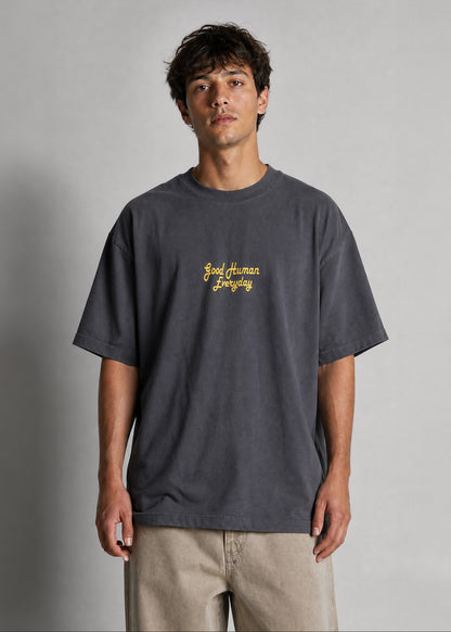 Man wearing a dark gray t-shirt with yellow text on a plain background