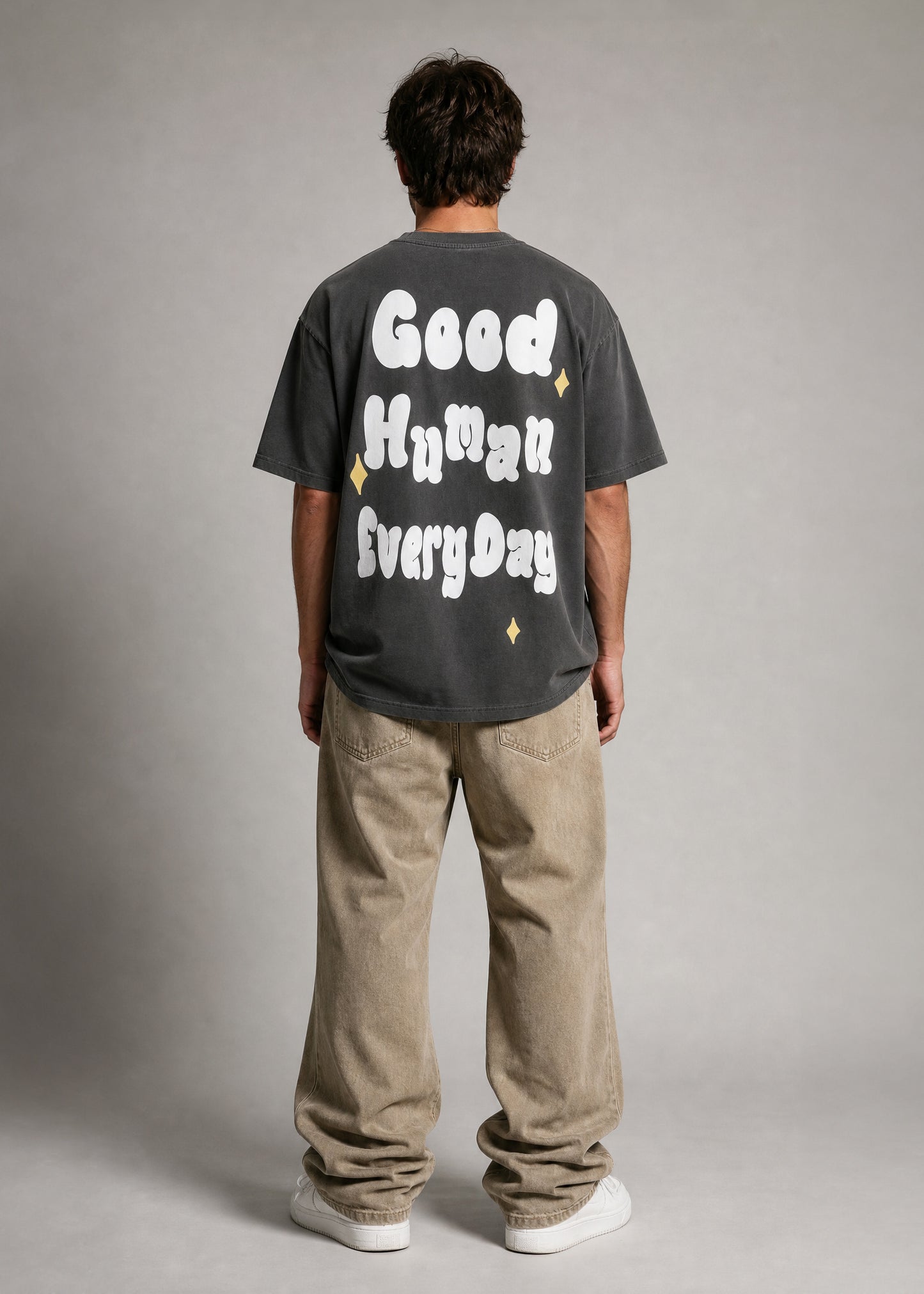 Person wearing a dark gray t-shirt with text on the back, standing against a plain background