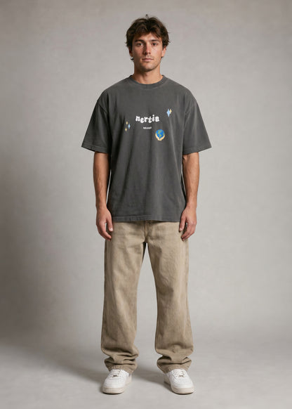 Man wearing a dark gray t-shirt with a logo and text, beige pants, and white shoes on a plain background