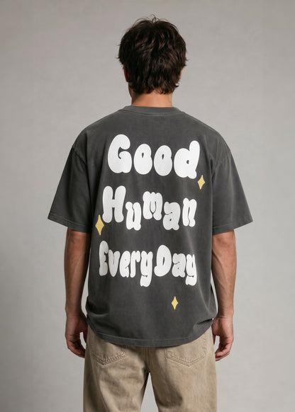 Person wearing a black t-shirt with 'Good Human Everyday' text on the back against a gray background