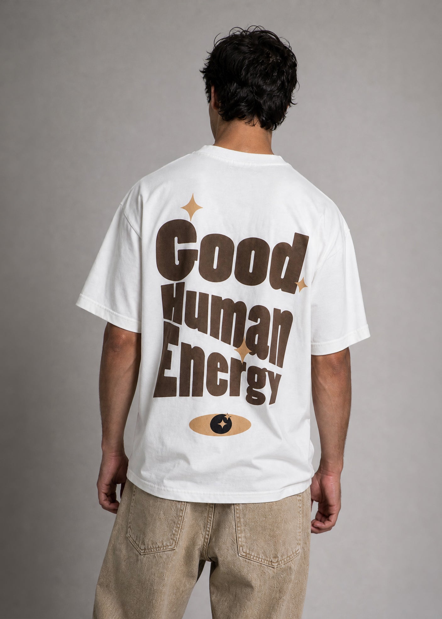 Person wearing a white t-shirt with 'Good Human Energy' text on the back against a gray background