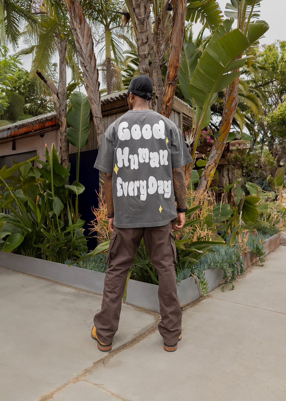 Person wearing a gray t-shirt with 'Good Human Every Day' text in a garden setting