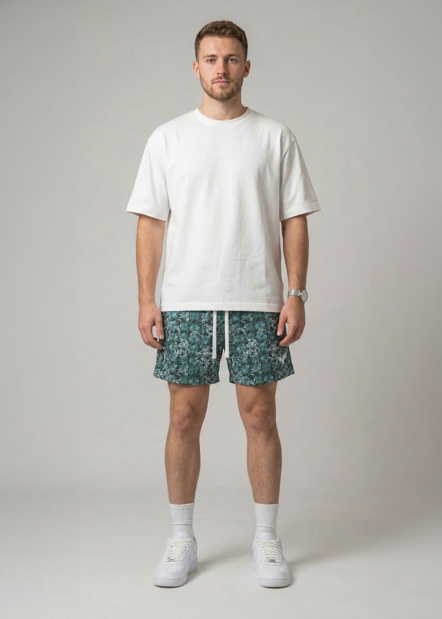 Man wearing a white t-shirt and patterned shorts on a plain background