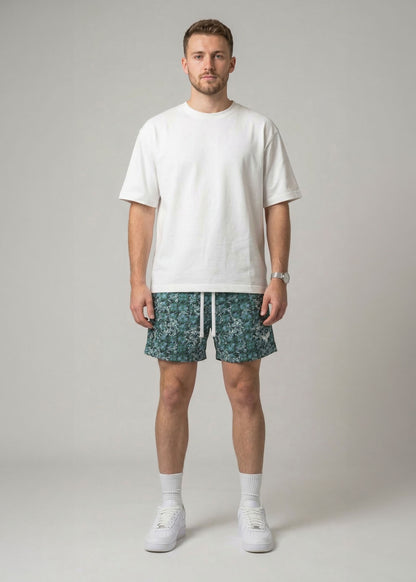 Man wearing a white t-shirt and patterned shorts on a plain background