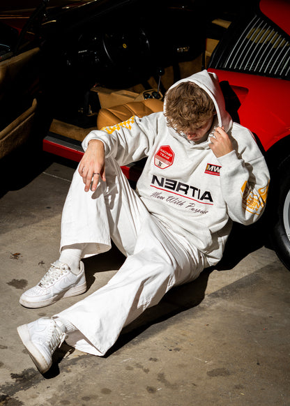 Person wearing a white hoodie with branding sitting on the ground next to a car.
