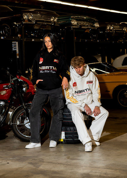 Two people wearing branded hoodies in a garage setting with vehicles in the background.