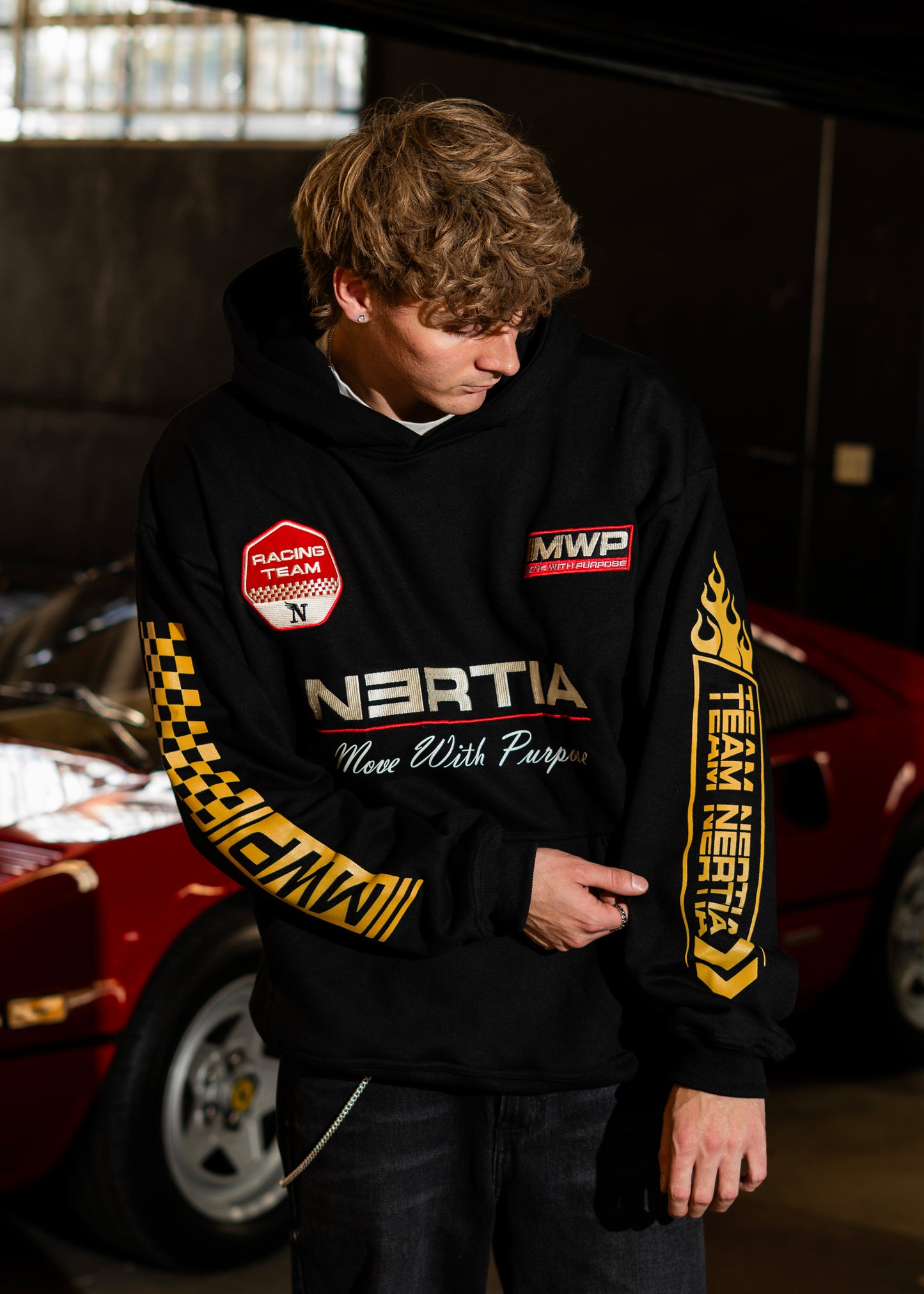 Person wearing a black hoodie with branding in front of a red car