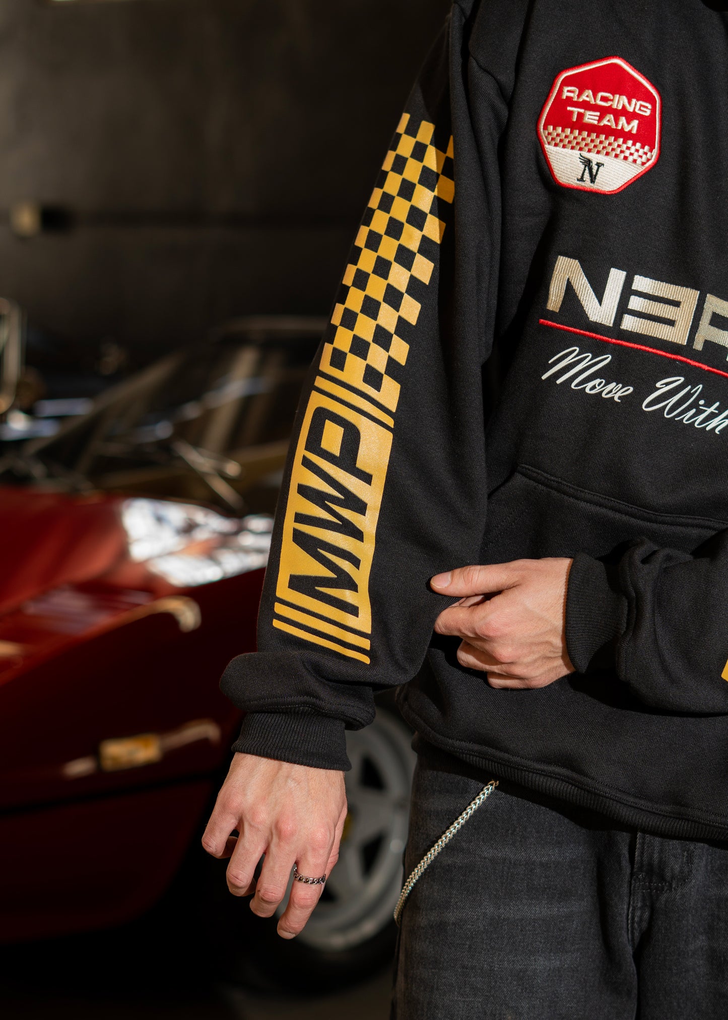 Person wearing a black hoodie with racing-themed designs and text, sitting next to a car.