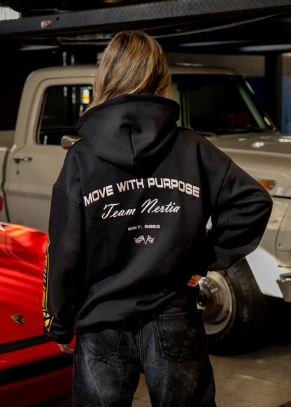 Person wearing a black hoodie with text, standing in front of a red car and beige truck.