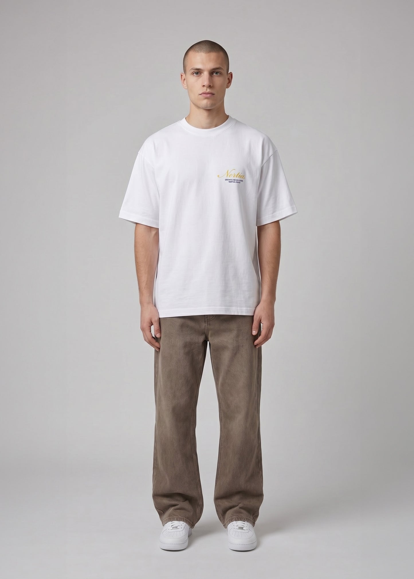 Man wearing a white t-shirt with a small logo and brown pants on a gray background