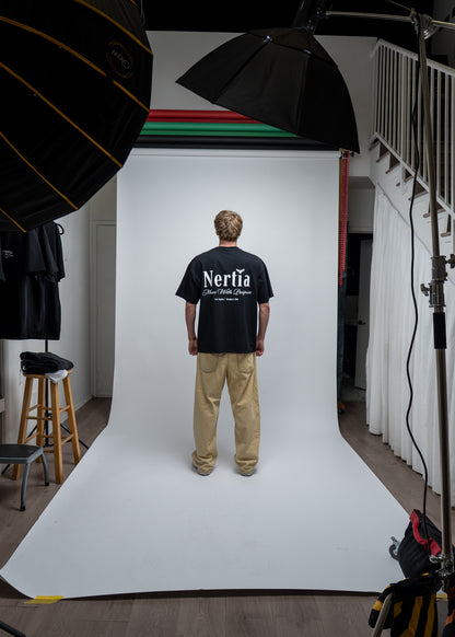 Person wearing a black 'Nertia' t-shirt standing in front of a white backdrop with photography equipment around.
