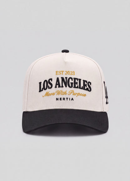 A structured baseball cap with an off-white crown and a black curved brim. The front features embroidered text reading 'EST 2023 LOS ANGELES More With Purpose NERTIA' in black and gold, with a small black embroidered LA logo on the side.