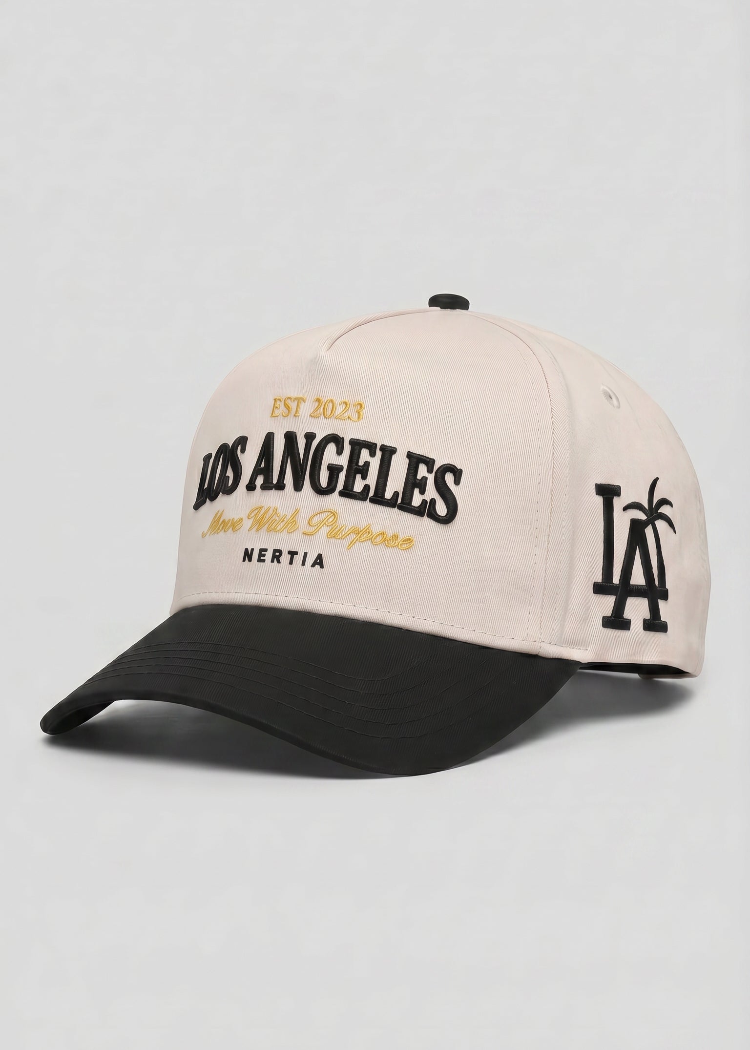 A baseball cap with a light beige crown and a black curved brim. The front features 'LOS ANGELES' embroidered in black with gold accents, and the side displays a black 'LA' logo with a palm tree.